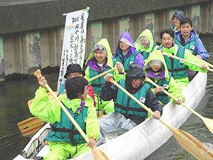 雨が降る中、10名の参加者がEボートに乗り全員で漕いでいる写真