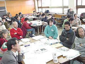 会議室内にグループに分かれて座っている参加者が、熱心に話しを聞いている写真