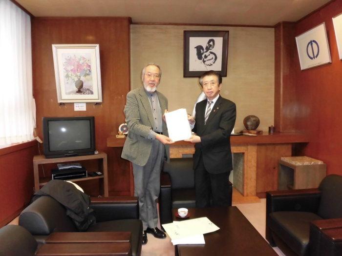 テーブルとソファーのある部屋で増田会長（左側）と北川市長（右側）が報告書を一緒に持ち記念撮影している写真
