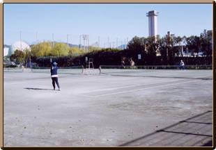 晴天の下、市民テニスコートで人々がテニスをしている写真