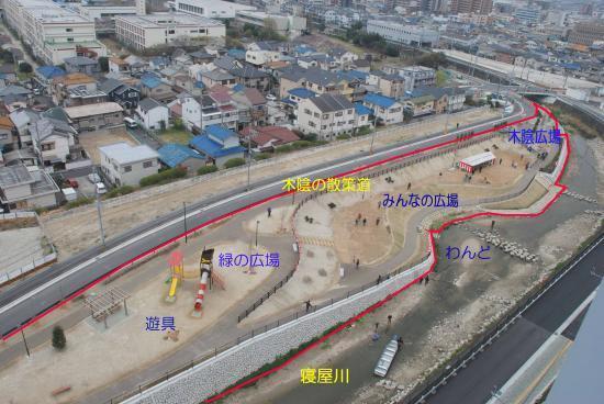 遊具、緑の広場、木陰の散歩道、みんなの広場、木陰広場がある幸町公園があり、公園の道路沿い側は住宅街が広がり、寝屋川沿い側がわんどになっている様子を上空から撮影した写真