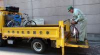 黄色いトラックの撤去車に放置された自転車を積んでいる作業服姿の男性の写真