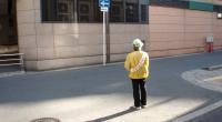 帽子を着用しタスキをかけた啓発員が道路に立っている写真