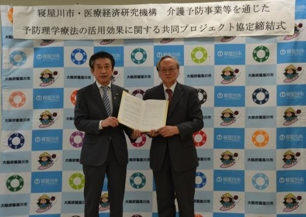 市長と医療経済研究機構所長（西村周三氏）が協定書を2人で持って写っている協定締結式の写真