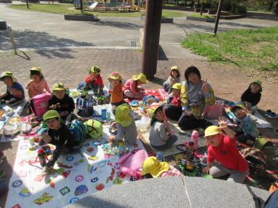 シートの上に座った子供たちや保育士がお弁当を食べたり、ピースをしてポーズととっている写真