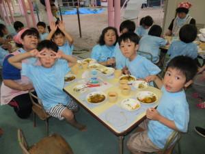 机の上にカレーライスが並んでいて、子供たちが座って食べている写真