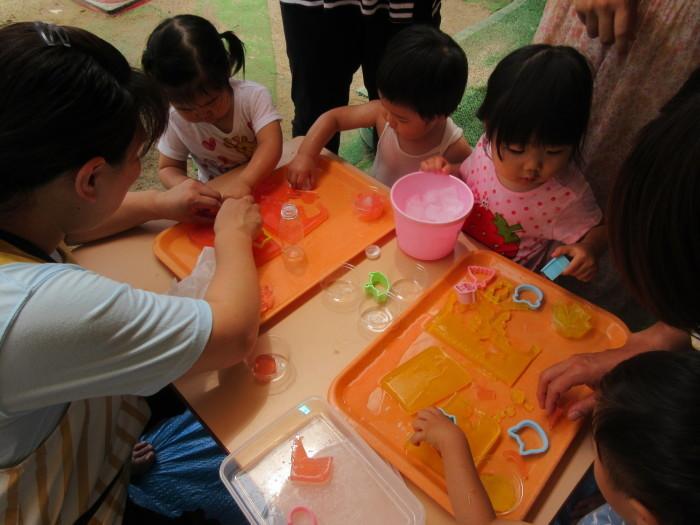 子供たちがオレンジのお盆の上に置かれた寒天で型抜きをして遊んでいる写真