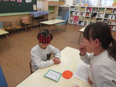 目隠しをした男の子の前で女性がお菓子のようなものをくわえている写真