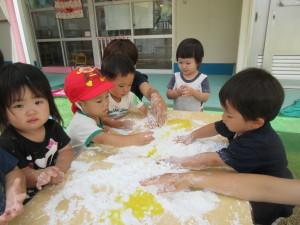 机の上一面に片栗粉が敷かれていて、子供たちが手を片栗粉の中に入れて遊んでいる写真