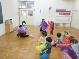 子供たちが床の上に座っていて、色とりどりの薄い布を広げて遊んでいる写真