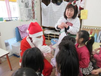 サンタクロースの周りに子供たちが集まっていて、手前にいる子供の手をサンタクロースが握っている写真
