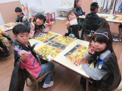お菓子を持った男の子2人と猫耳をつけた女の子2人が机に座りながらポーズをとっている写真