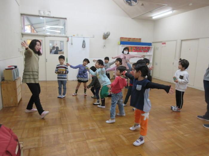 12人ほどの子供たちが前に立っている女性の真似をしながら両手を伸ばしてポーズをとっている写真