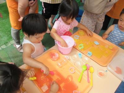 寒天をスプーンでさわる男の子、その横でバケツに手を入れて遊んでいる女の子が写っている写真