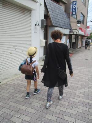 制服を着た幼稚園児と子育てサポーターの女性が並んで歩いている後ろ姿の写真