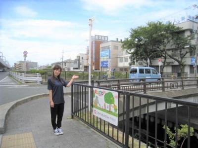 橋の手前にあるフェンスにあるRELATTOの看板を指している女性の写真