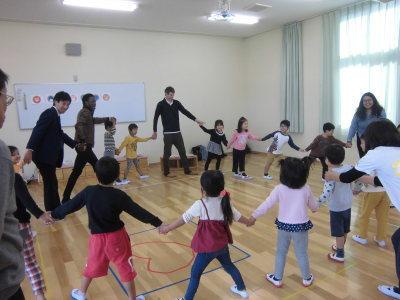 園児と先生方がてをつなぎ円をつくって踊りを踊っている写真