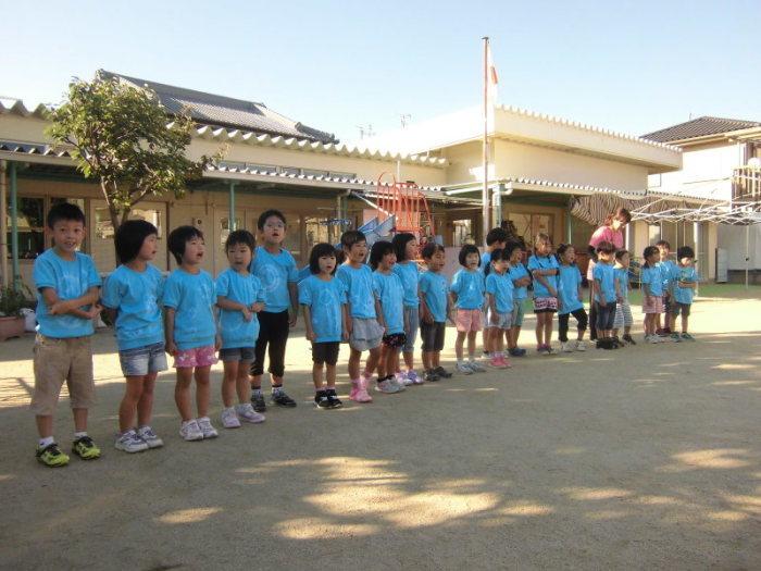 お揃いの水色の絞り染めのティーシャツを着て、園庭で横一列に並んで立っている子供たちの写真