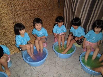 タライに入ったお湯に足をつけて足湯をしている子供たちの写真