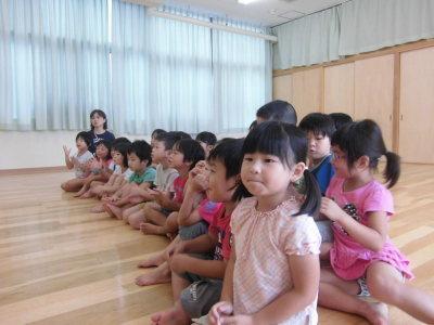 床に横一列に並んで座って末吉先生の話を聞いている子供たちの写真