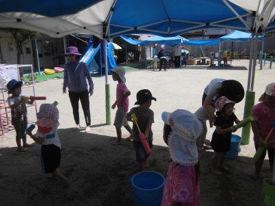 テントの日陰で水鉄砲で遊ぶ園児達の写真