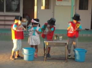 赤いベストの男の子3人と白いベストの女の子が水がはいったビニール袋を持っている写真