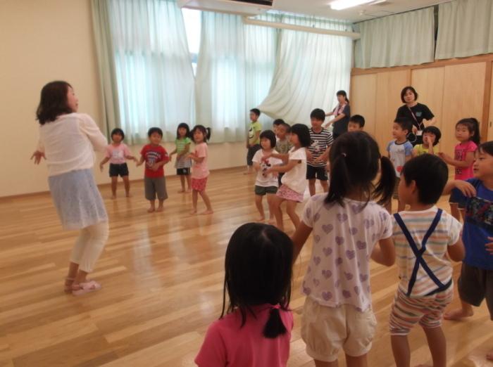 膝を曲げて体を傾けてダンスをしている先生と先生の真似をして踊っている子供たちの写真