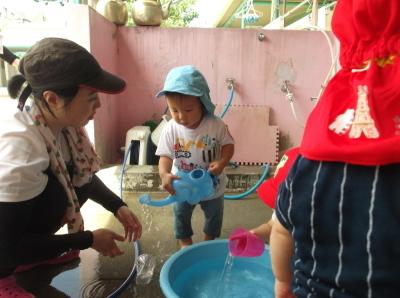 水色の象の形のじょうろで遊んでいる子供と傍で見ている先生の写真