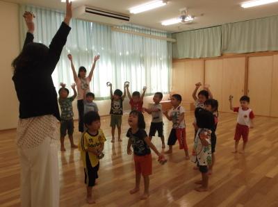 鈴を振ってダンスをしている子供たちと両手を上に挙げている先生の写真