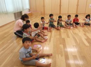 床に円を描くように座って両手に太鼓のばちを持っている子供たちの写真
