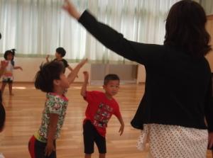 両手を広げ体を揺らしてダンスをしている子供たちと先生の写真