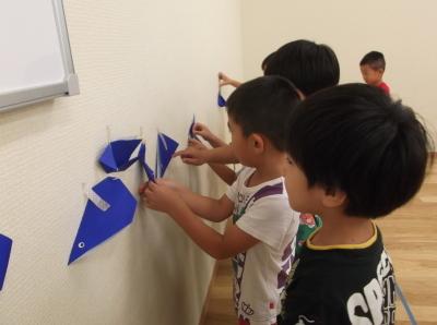 折り紙で作った魚を壁に貼っている子供たちの写真
