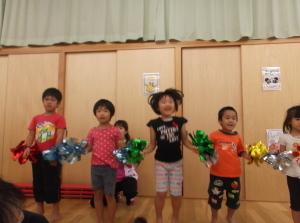 赤や黄色や緑色のカラフルなポンポンをもって飛び跳ねながら踊っている子供たちの写真