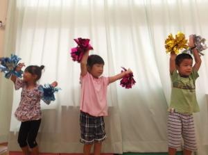 ポンポンを持った両手を挙げてダンスを踊っている子供たちの写真
