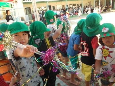両端にカラフルなテープがついた棒を持っている緑色の帽子をかぶった子供たちの写真