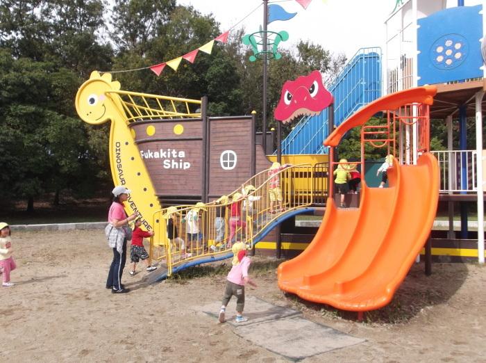 オレンジ色の滑り台がついている、恐竜がモチーフの遊具で遊んでいる子供たちの写真