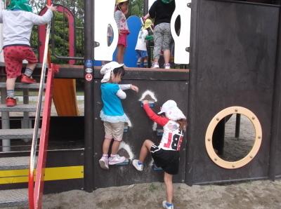 遊具の壁をよじ登って遊んでいる子供たち、遊具の階段を登っている子供の写真