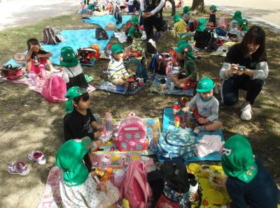 芝生にレジャーシートを敷いてお弁当を食べている緑色の帽子の子供たちの写真
