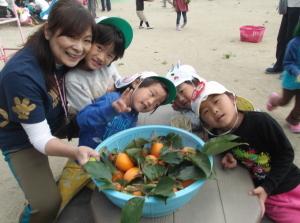 かごいっぱいに入った柿と4人の子供たち、先生の写真