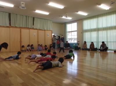 床に腹ばいに寝そべっている子供たち、部屋の端に並んで座っている子供たちと保護者の写真