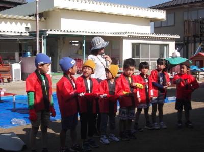赤い法被を着て横一列に並んで立っている子供たちと先生の写真