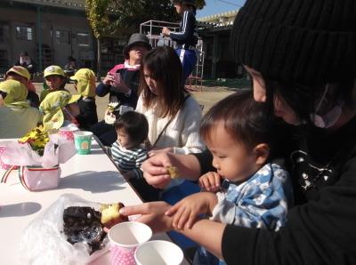 母親の膝の上でやきいもを食べている子供たちの写真