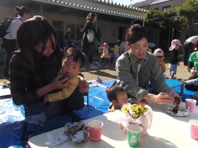 抱っこした子供にやきいもを食べさせている母親とやきいもの皮をむいている母親の写真