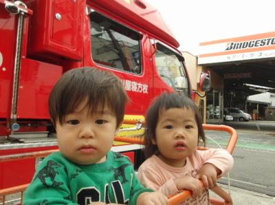 消防車をバックに散歩用のバギーに乗っている2人の子供の写真
