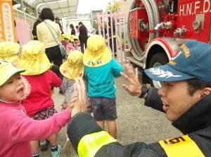 消防士とハイタッチをしている子供と消防車を見ている子供たちの写真