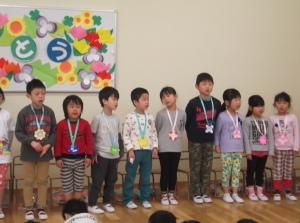 折り紙で作ったメダルを首から下げて横一列に並んで立っている子供たちの写真