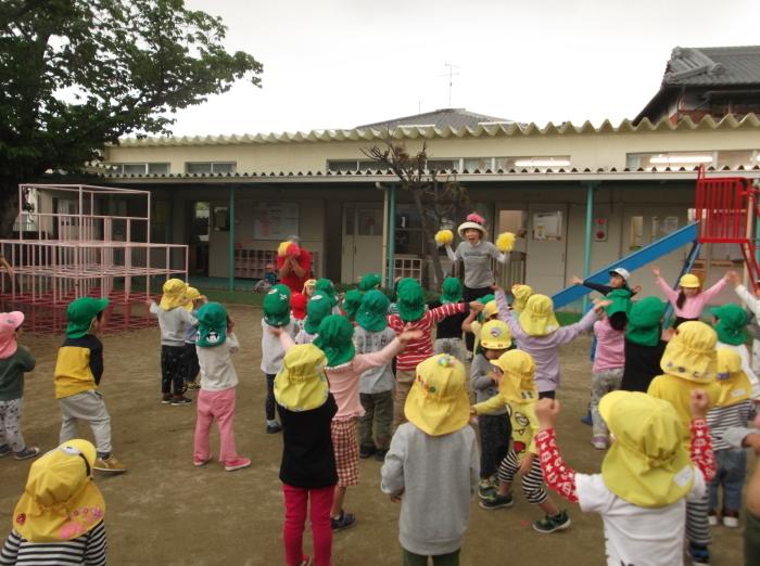 黄色の帽子を緑の帽子の園児達が園庭で先生と体操をしている写真