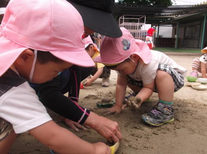 砂場にしゃがみ込んで真剣に泥団子を作っているピンク色の帽子を被った子供たちの写真