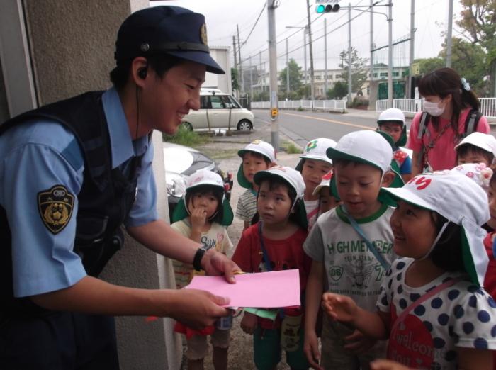 派出所を訪れた子供たちと先生、子供たちからの手紙を笑顔で受け取る警察官の写真