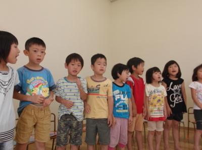 横一列に並んで立ち、歌を歌っている子供たちの写真